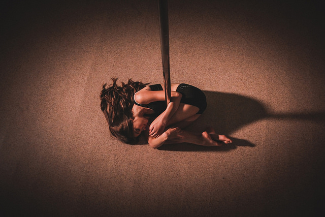 Pole dancer curled around base of the pole