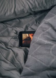 A phone showing an adult video playing half tucked under the bedclothes