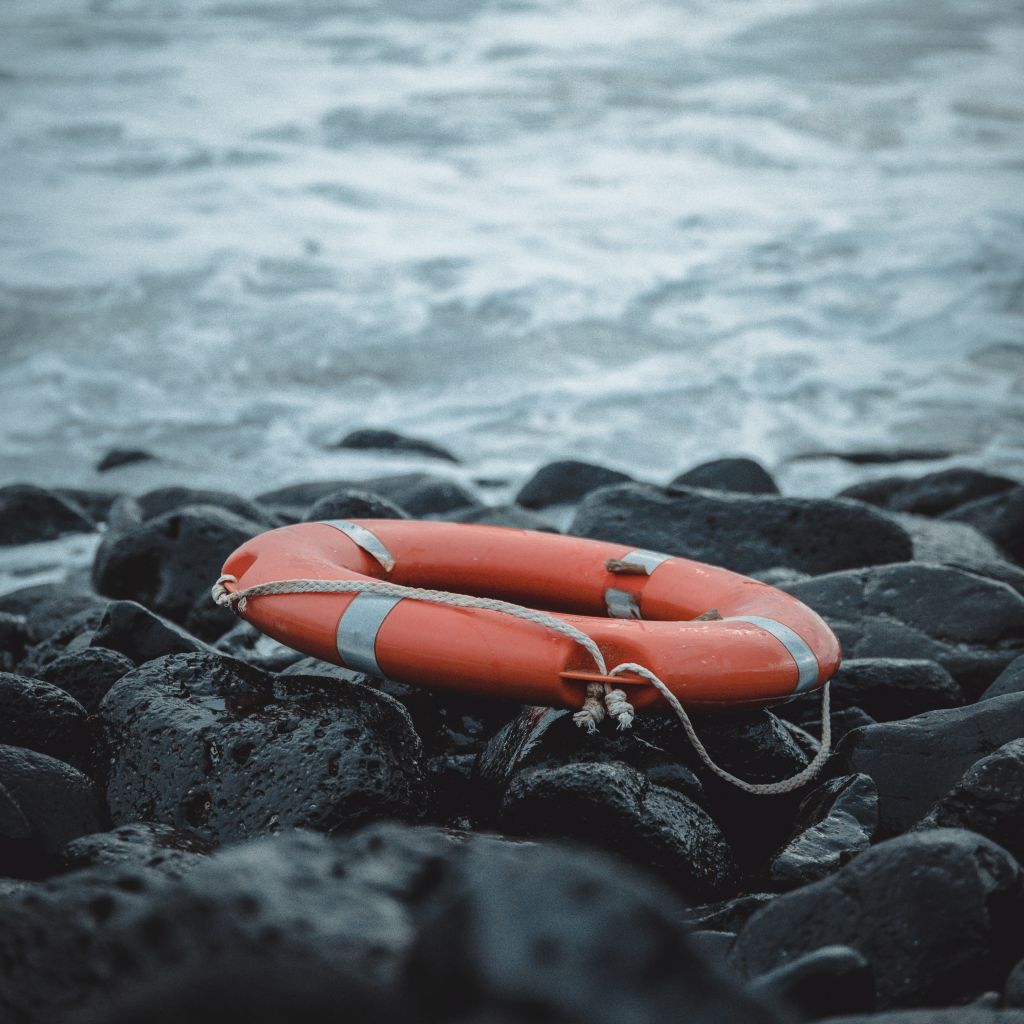Image of an orange rescue ring left stranded on the rocks on the edge of rough seas